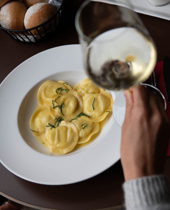 Hausgemachte Ravioli auf weissem Teller, dazu ein Glas Weisswein