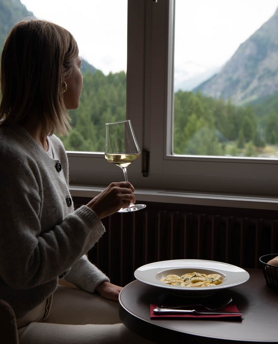 Gast geniesst Weisswein am Fenster mit Blick auf die Berge